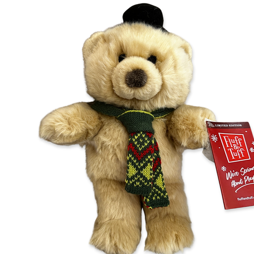 A plush dog toy shaped like a teddy bear. It's in a "standing" position with straight legs and arms sticking straight out at the side. It's made from a plush light brown fabric with a brown nose and eyes stitched in with black thread. It's wearing a dark green knitted scarf with a light green and red pattern in it. It's also wearing a small black plush top hat.